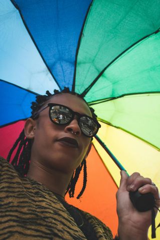 A stylish adult with sunglasses and a rainbow umbrella, showcasing bold fashion and expression.
